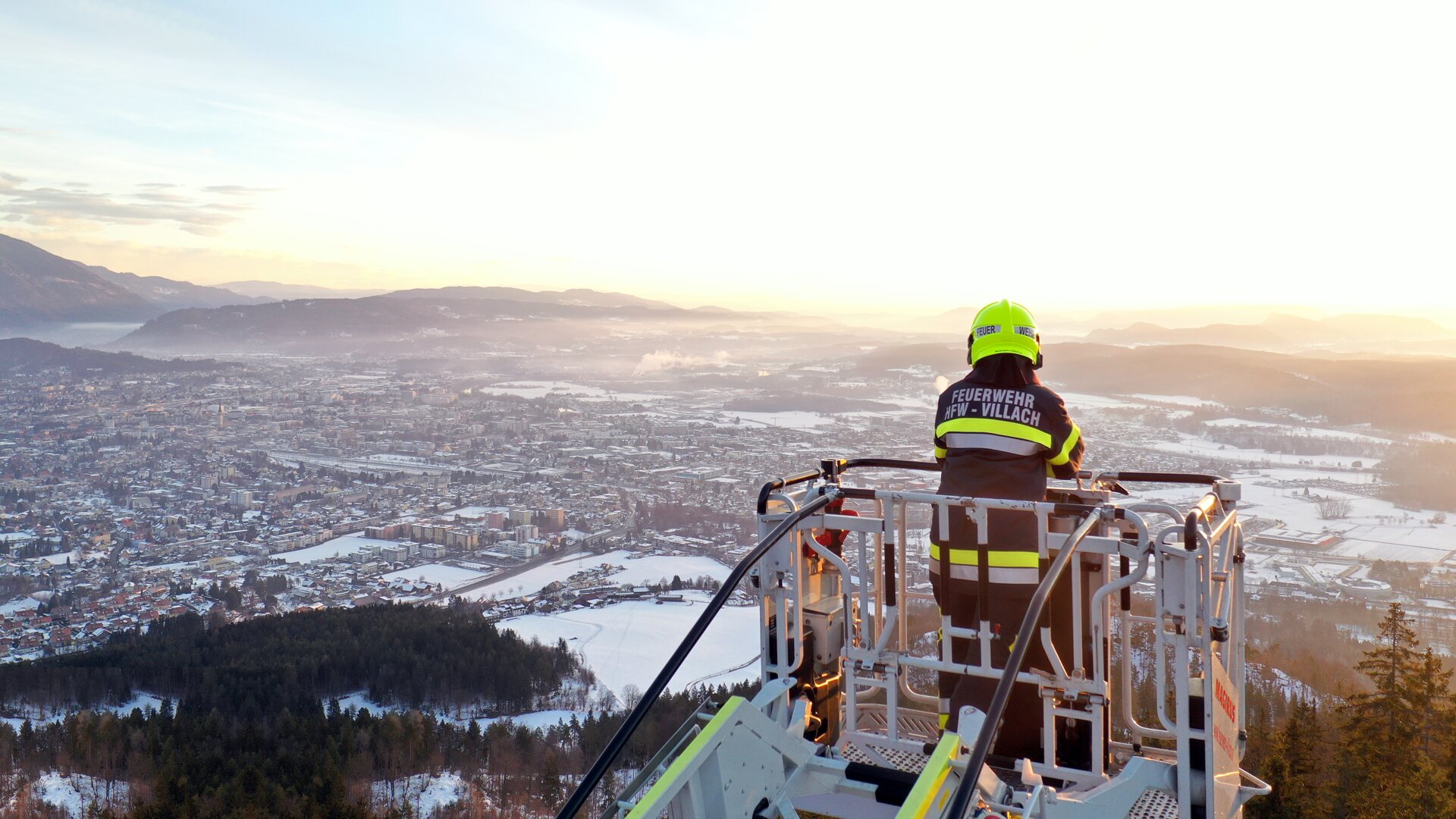 Feuerwehrmann im Drehleiterkorb über dem verschneiten Villach